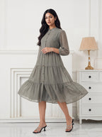 Woman wearing a green checkered dress in a white room with a lamp and dresser.