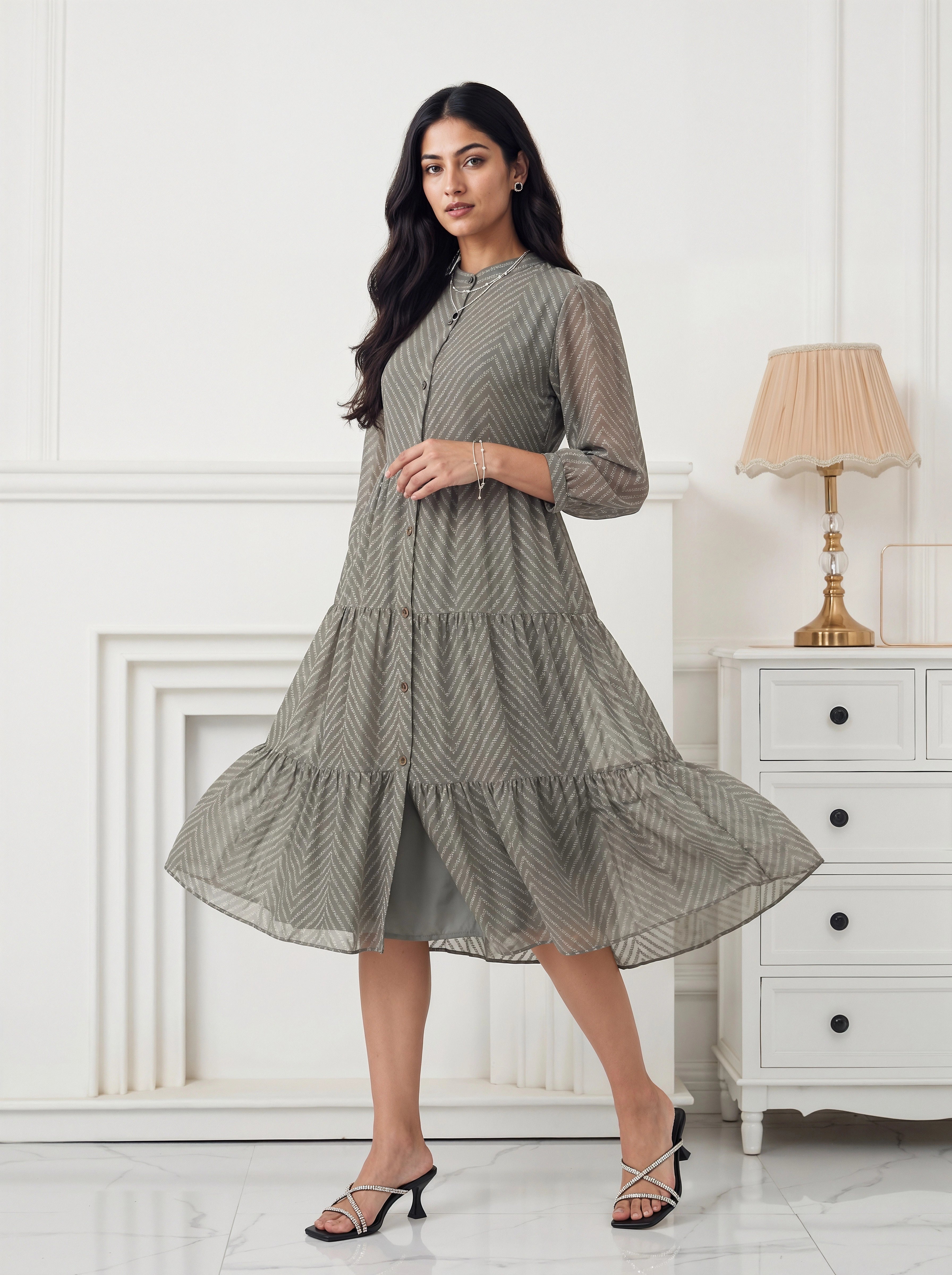 Woman wearing a green checkered dress in a white room with a lamp and dresser.