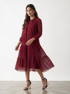 Woman wearing a burgundy dress with sheer sleeves against a white background
