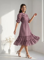 Woman wearing a flowy mauve tiered dress next to a vase with dried flowers