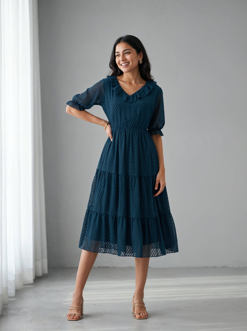 Woman wearing a dark blue dress standing in a room with white curtains.