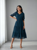 Woman wearing a dark blue dress standing in a room with white curtains.