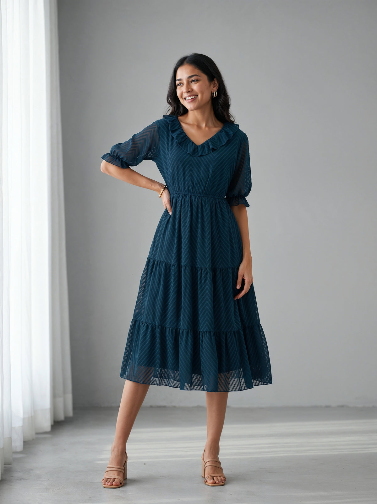 Woman wearing a dark blue dress standing in a room with white curtains.