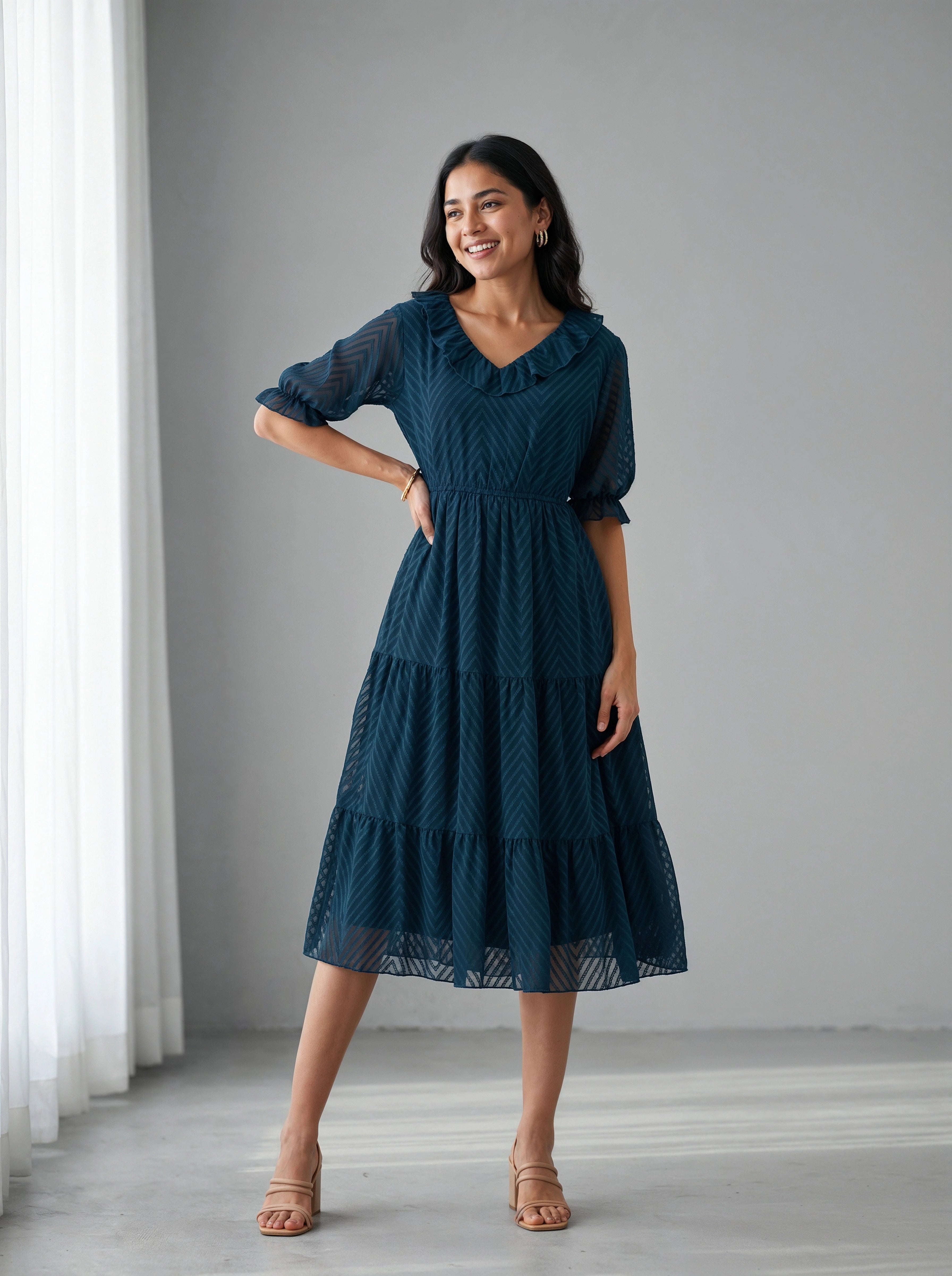 Woman wearing a dark blue dress standing in a room with white curtains.