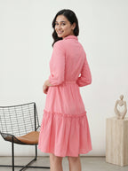 Woman wearing a pink dress in a minimalistic room with a chair and sculpture.