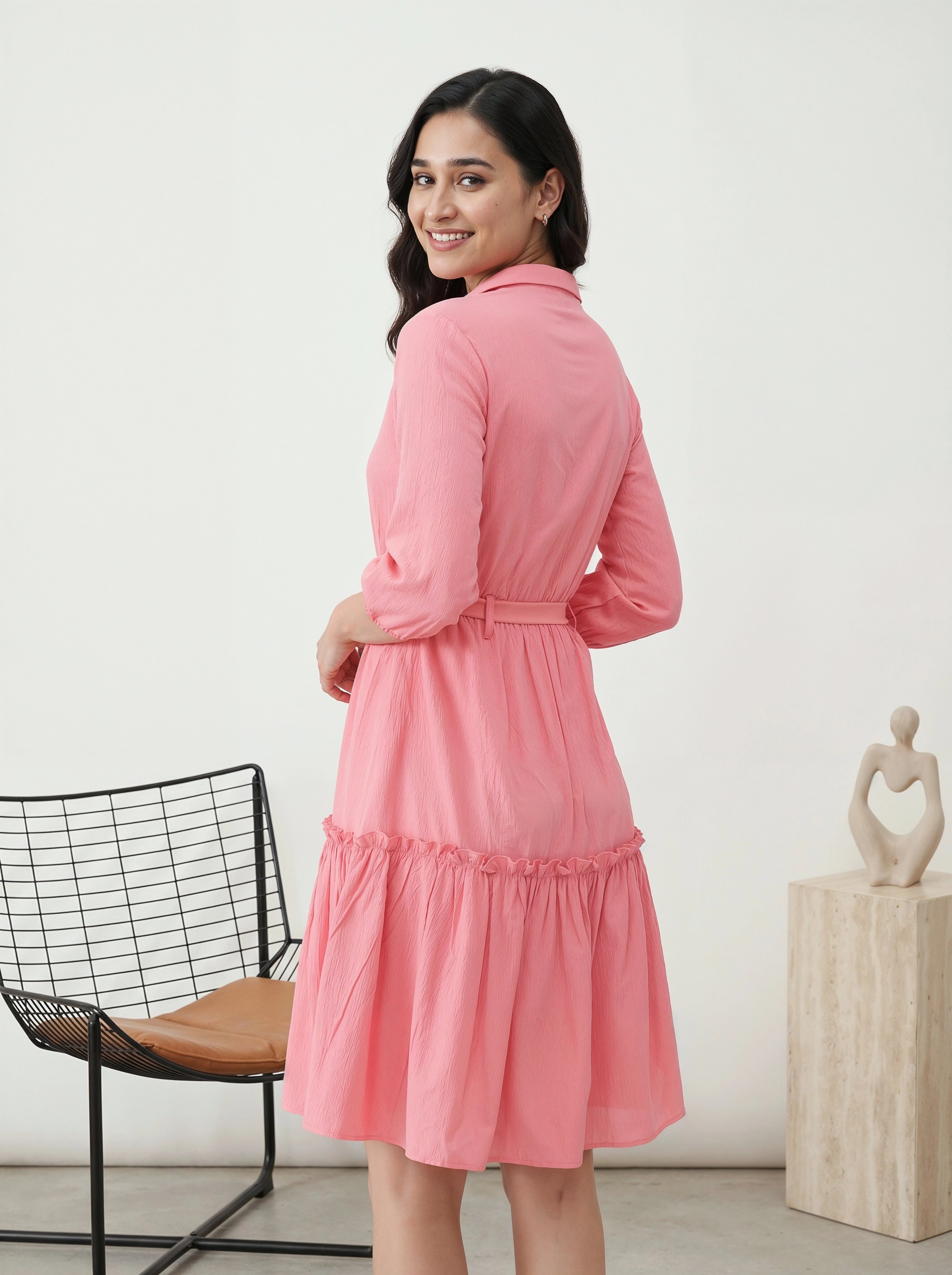 Woman wearing a pink dress in a minimalistic room with a chair and sculpture.