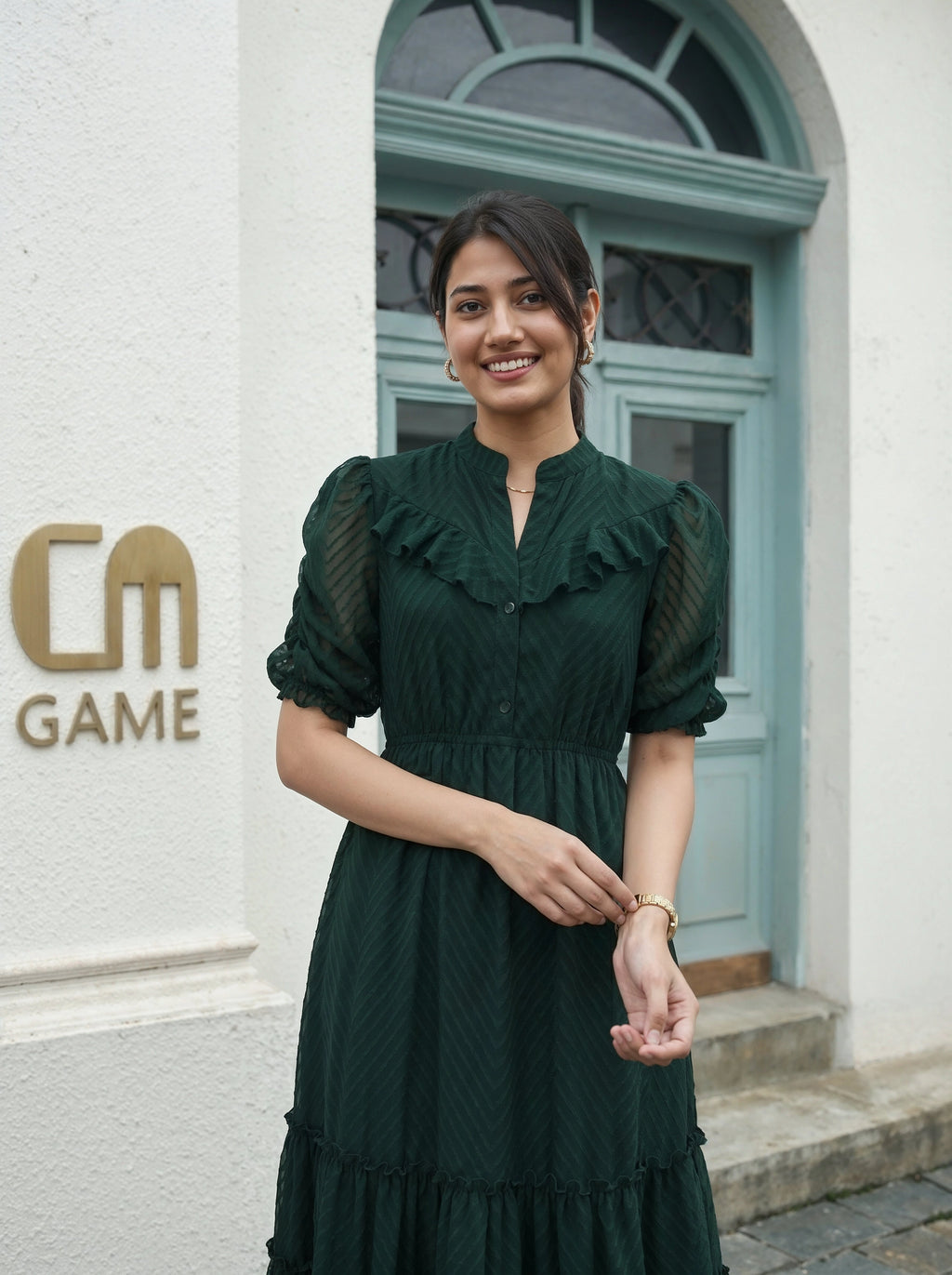 Woman in a green dress standing in front of a building with 'CM Game' logo.