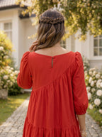 Woman in a red dress with braided hair standing in a garden.