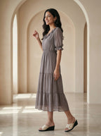 Woman in a gray dress standing in a sunlit room with arches