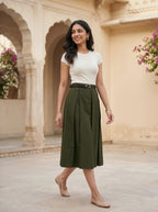 Woman in a white top and green skirt standing in an architectural setting with floral decorations.