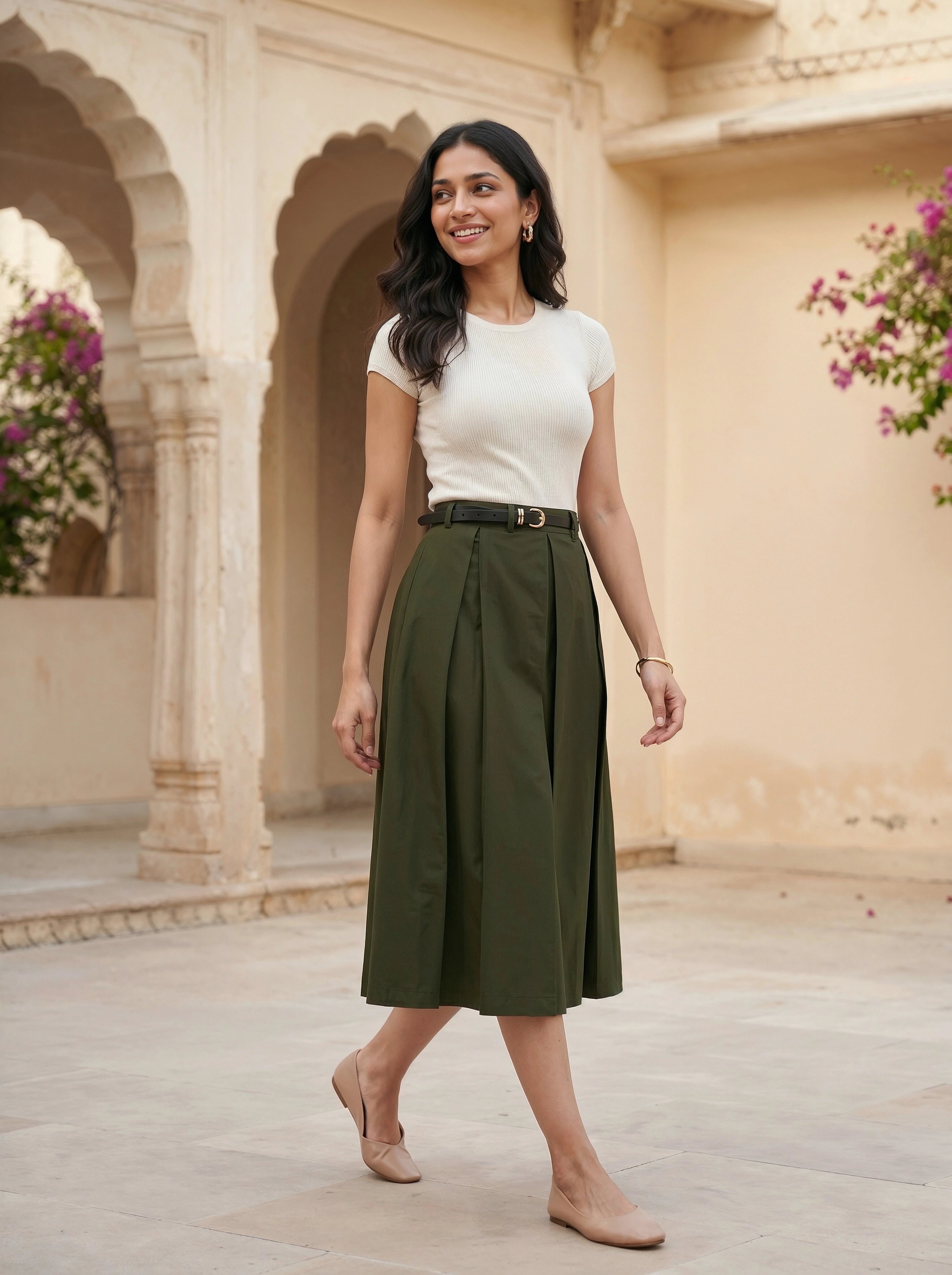 Woman in a white top and green skirt standing in an architectural setting with floral decorations.