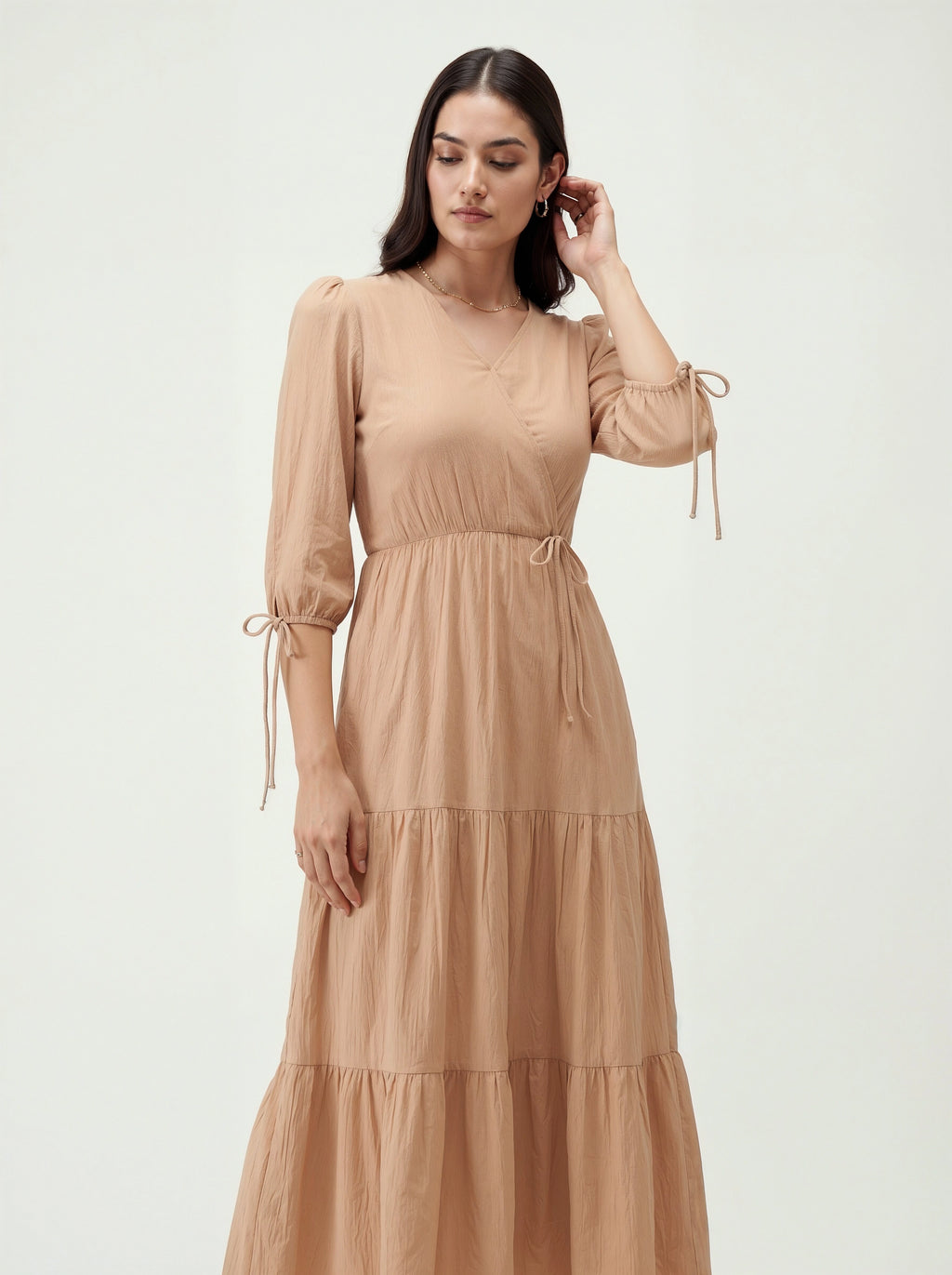 Woman wearing a beige dress with long sleeves and tiered skirt on a white background
