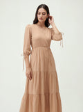 Woman wearing a beige dress with long sleeves and tiered skirt on a white background