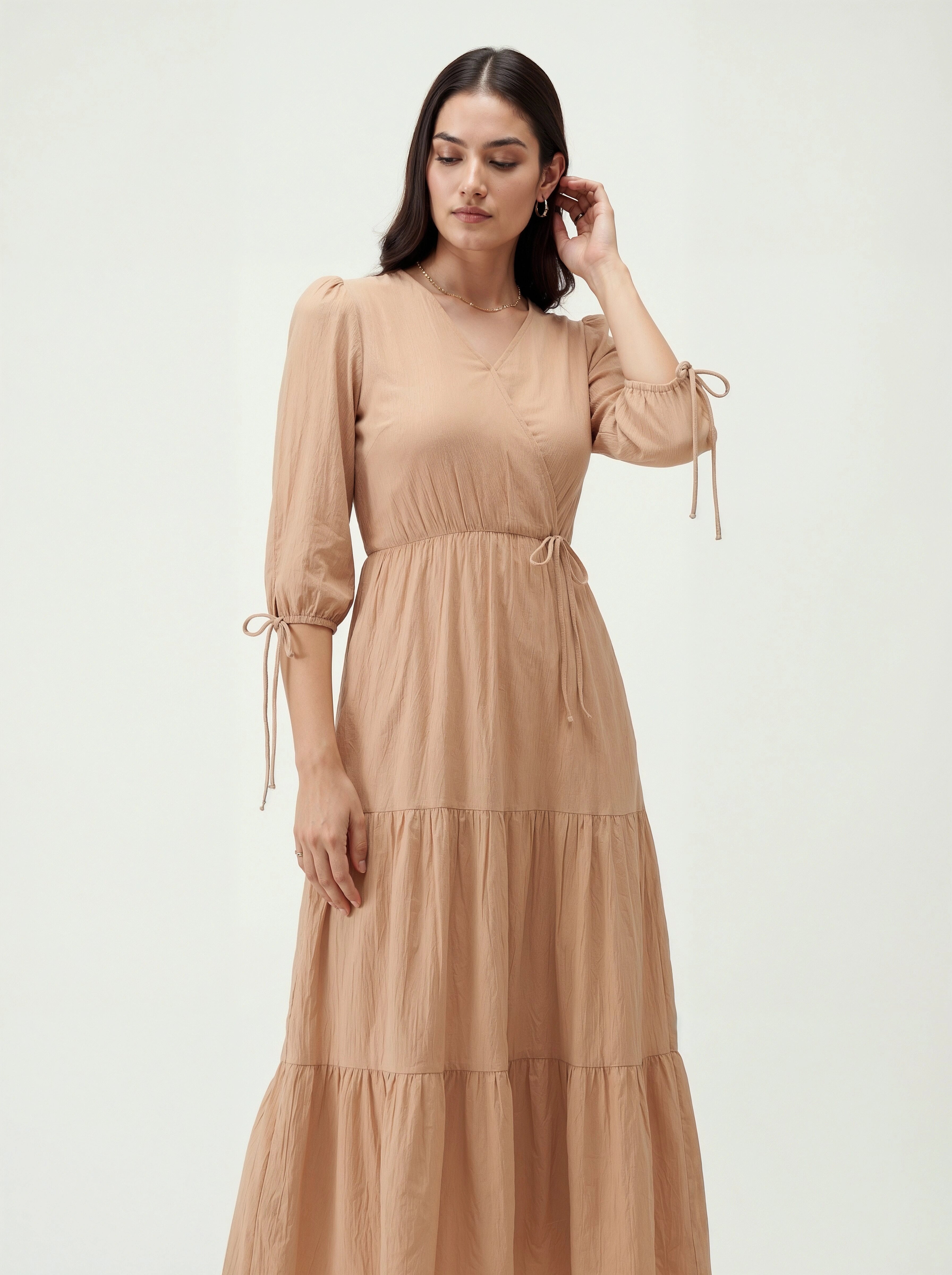 Woman wearing a beige dress with long sleeves and tiered skirt on a white background