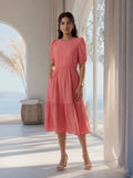 Woman in a pink dress standing in a bright room with large windows and a view of the ocean.