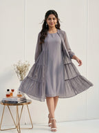 Woman wearing a gray dress with a matching cardigan in a minimalistic setting.