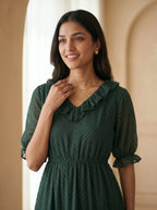 Woman wearing a green dress with a ruffled neckline against a beige wall.
