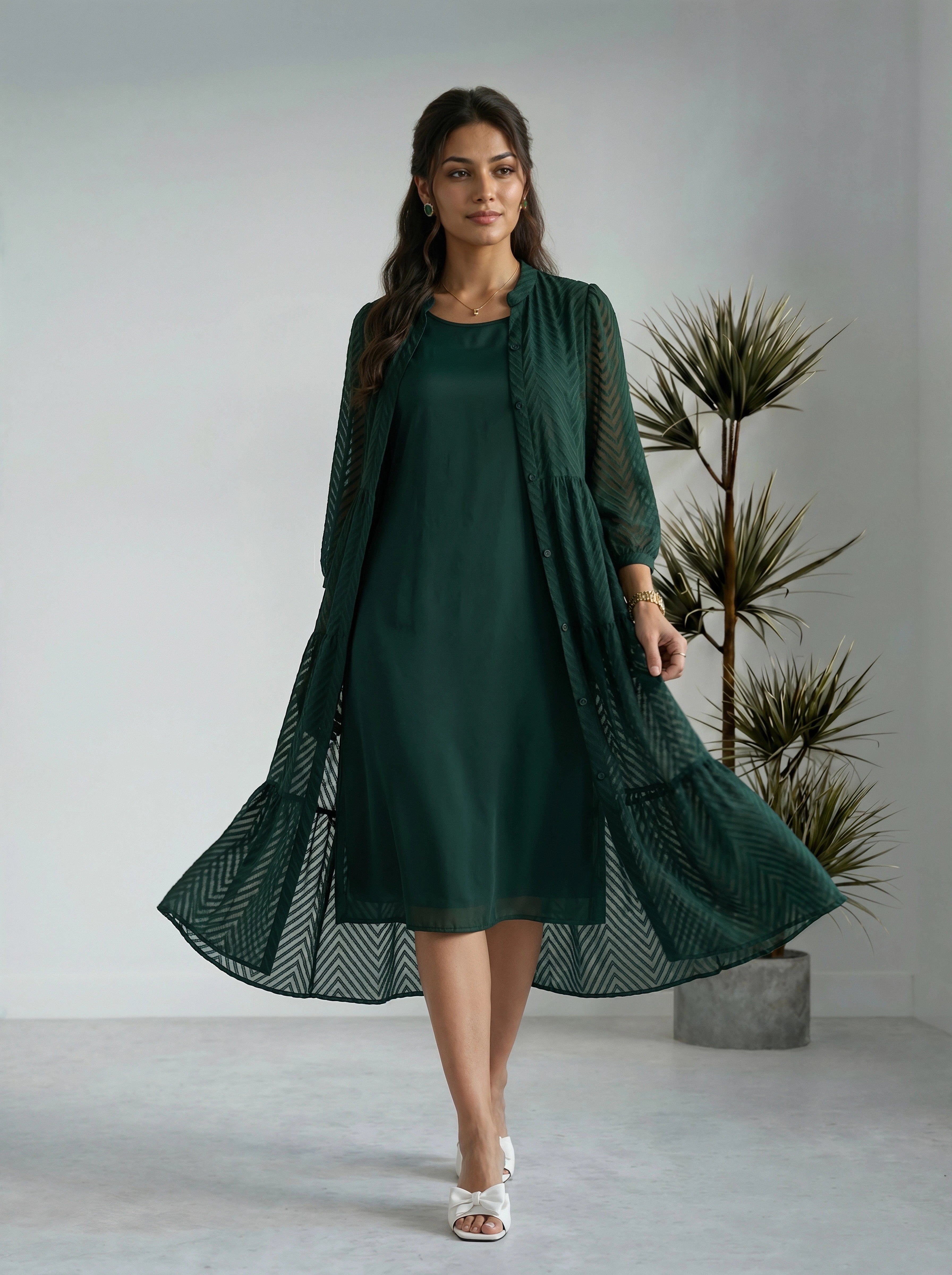 Woman wearing a green dress with a matching cardigan in a minimalistic setting.