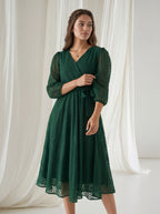 Woman wearing a green dress standing in front of white curtains