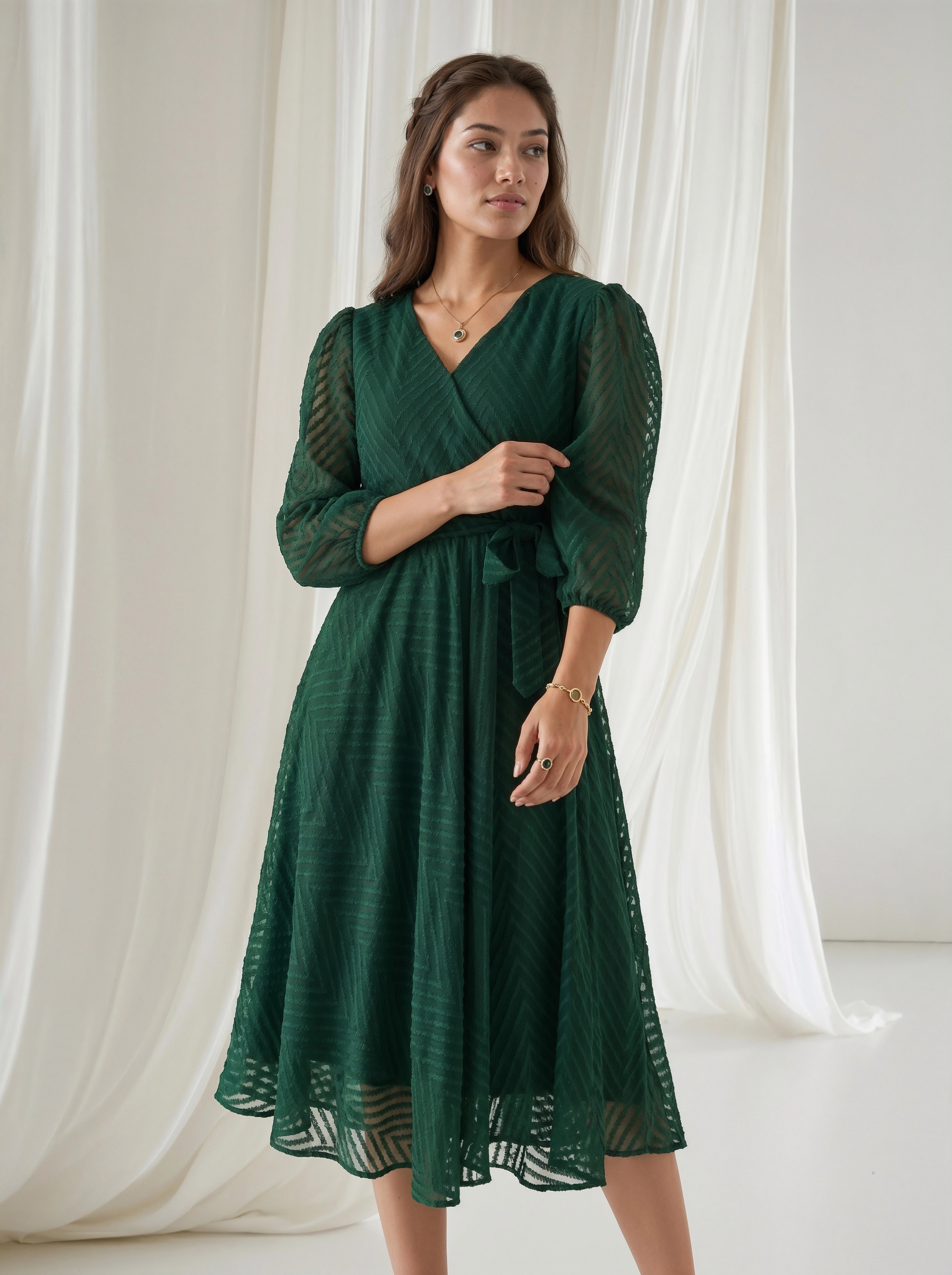 Woman wearing a green dress standing in front of white curtains