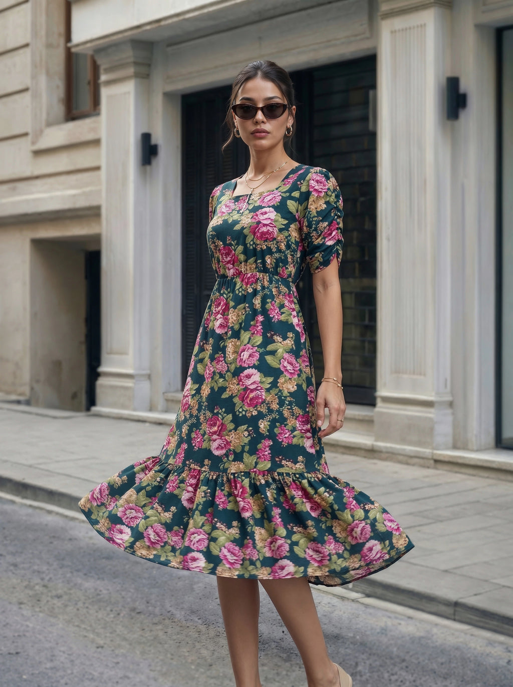 A woman wearing a short-sleeve midi dress with a dark green floral print featuring pink roses and green leaves, standing on a city street.