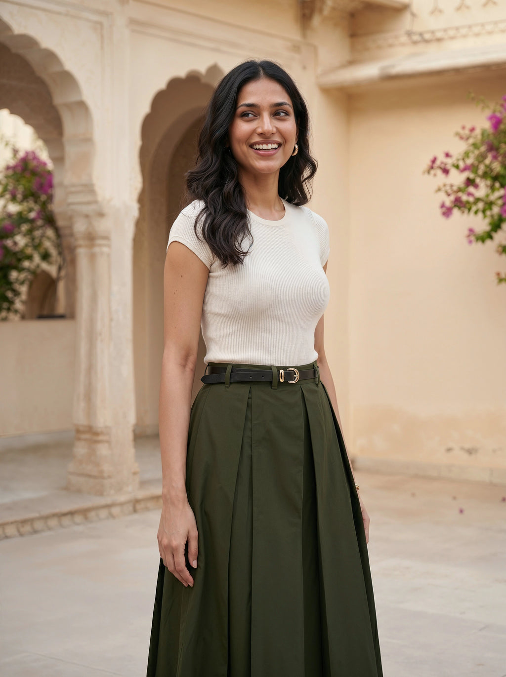 Woman in a white top and green skirt standing in an architectural setting with floral decorations.