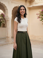 Woman in a white top and green skirt standing in an architectural setting with floral decorations.