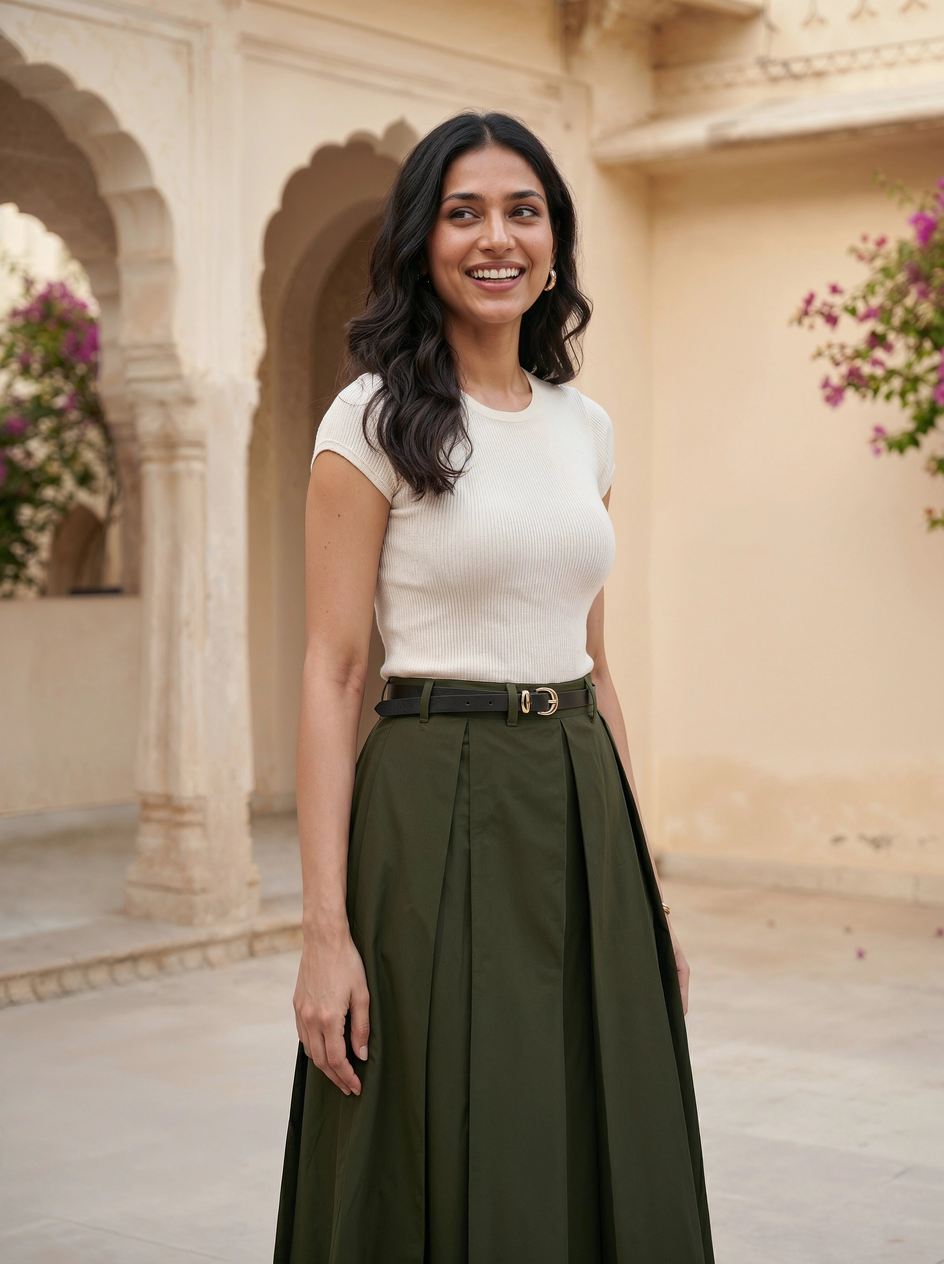 Woman in a white top and green skirt standing in an architectural setting with floral decorations.