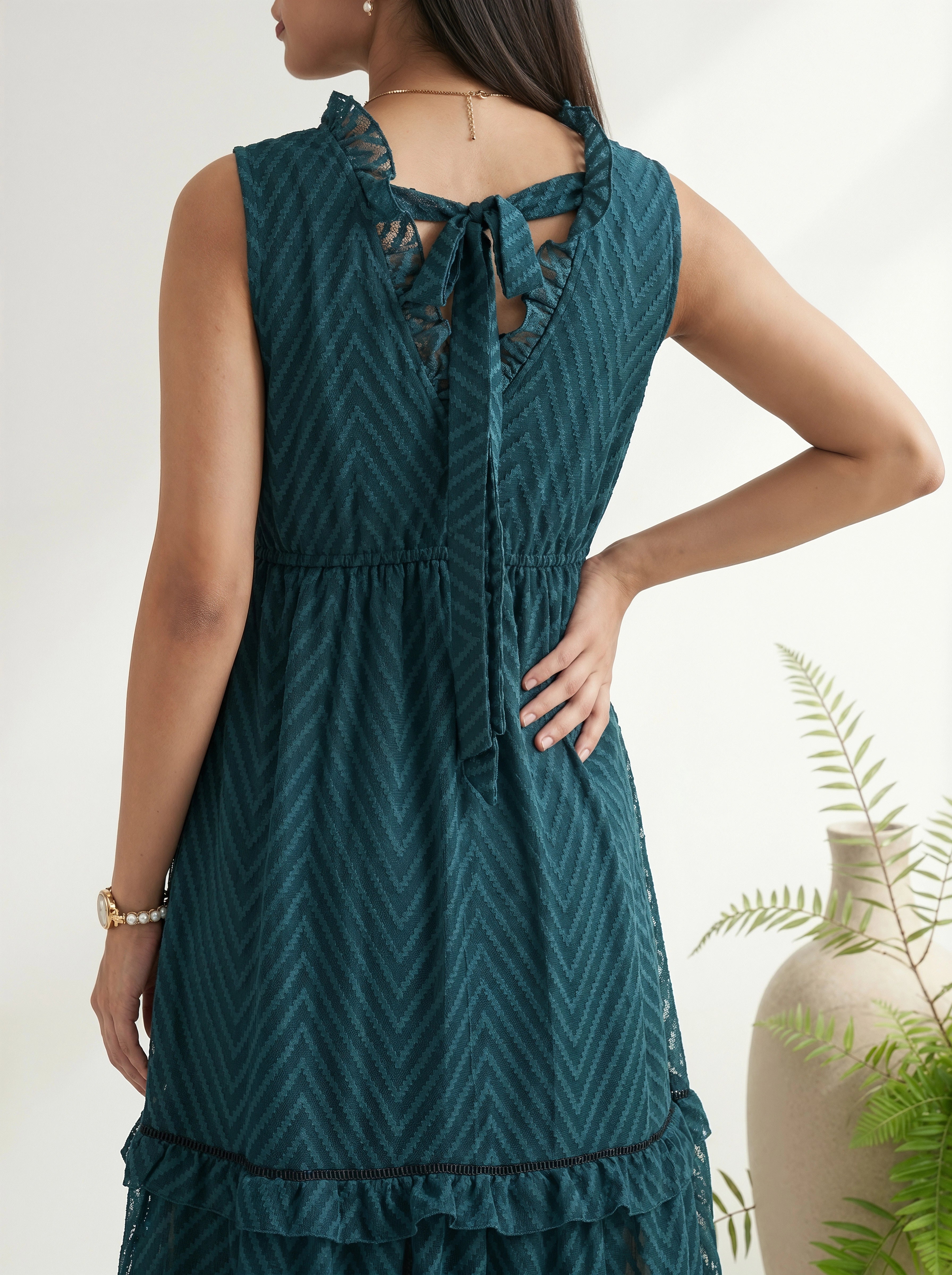 Woman wearing a teal dress with a geometric pattern, standing against a neutral background.
