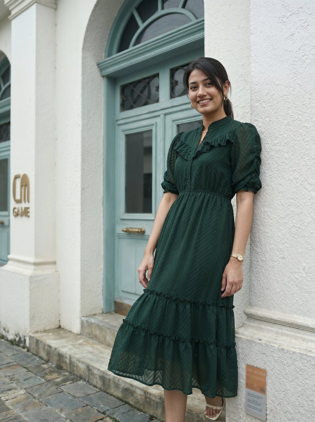 Woman in a green dress standing in front of a building with a blue door.