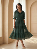 Woman wearing a green dress standing in a room with beige walls and floor.