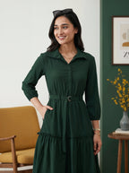Woman wearing a green dress in a room with a yellow couch and framed picture on the wall.