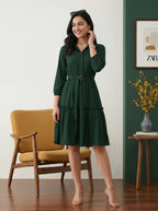Woman in a green dress standing in a room with a yellow chair and decorative elements.