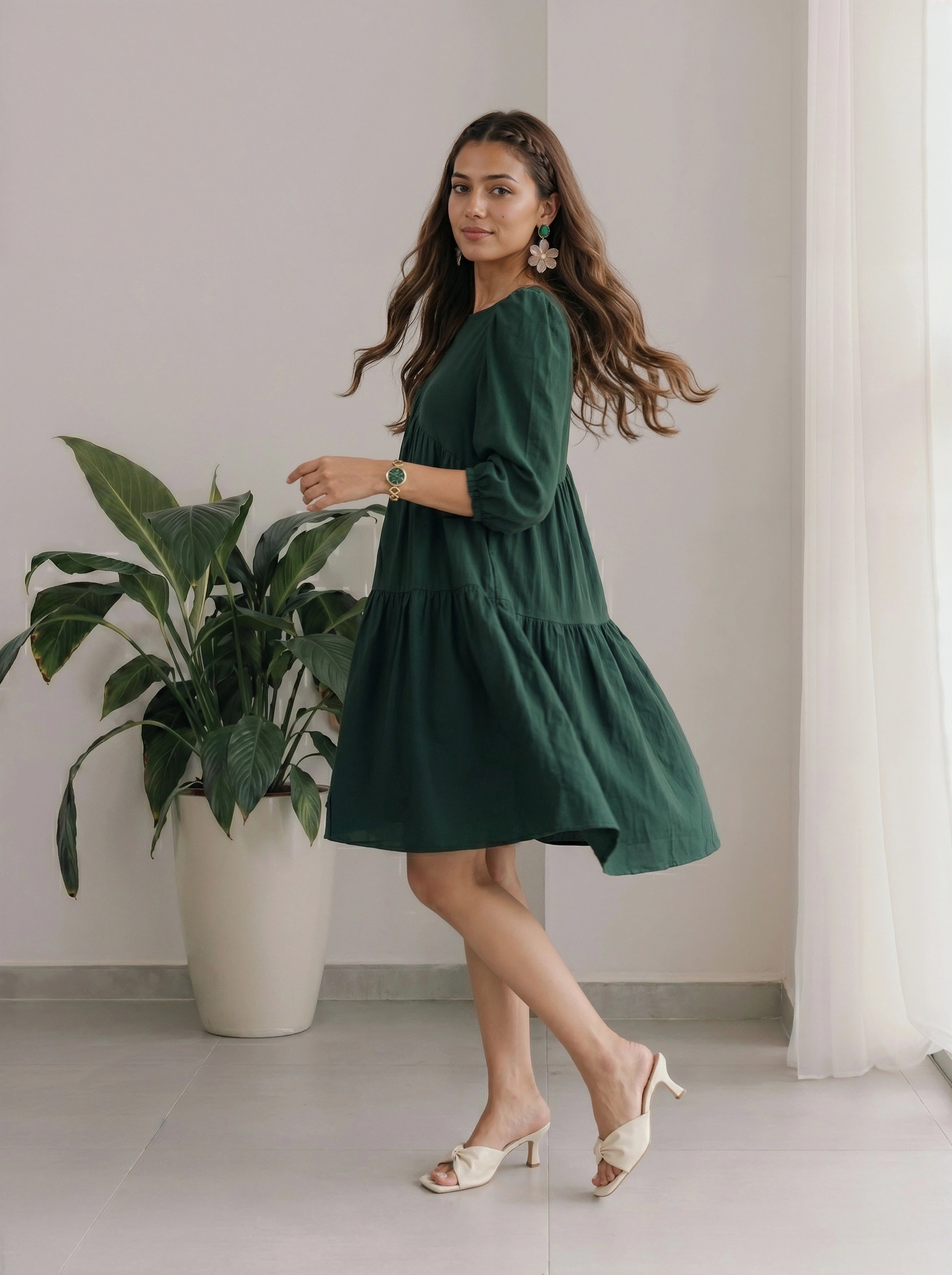 Woman in a green dress standing next to a plant indoors
