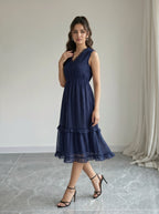 Woman wearing a navy blue dress standing in a room with a neutral background