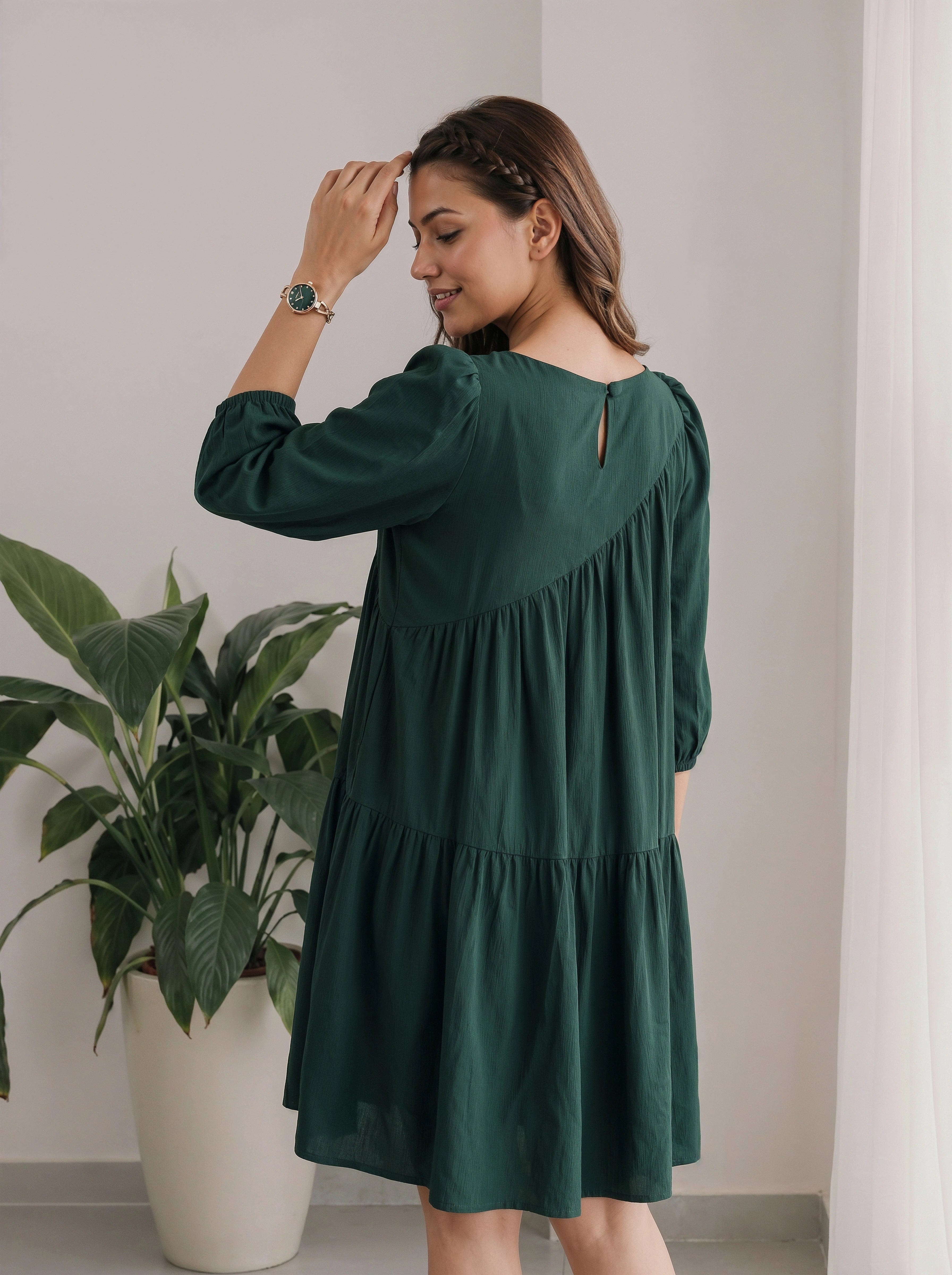 Woman wearing a green dress standing indoors with a plant in the background
