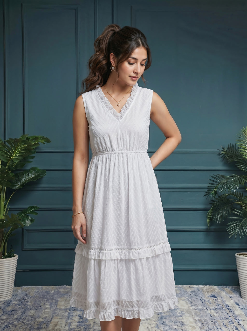 Woman wearing a white dress standing against a blue wall with plants.