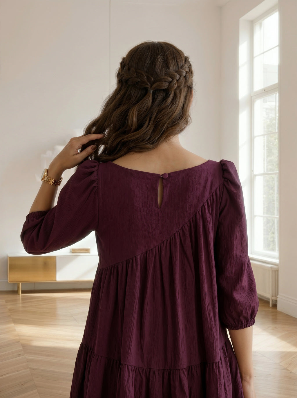 Woman in a burgundy dress standing in a room with a window in the background
