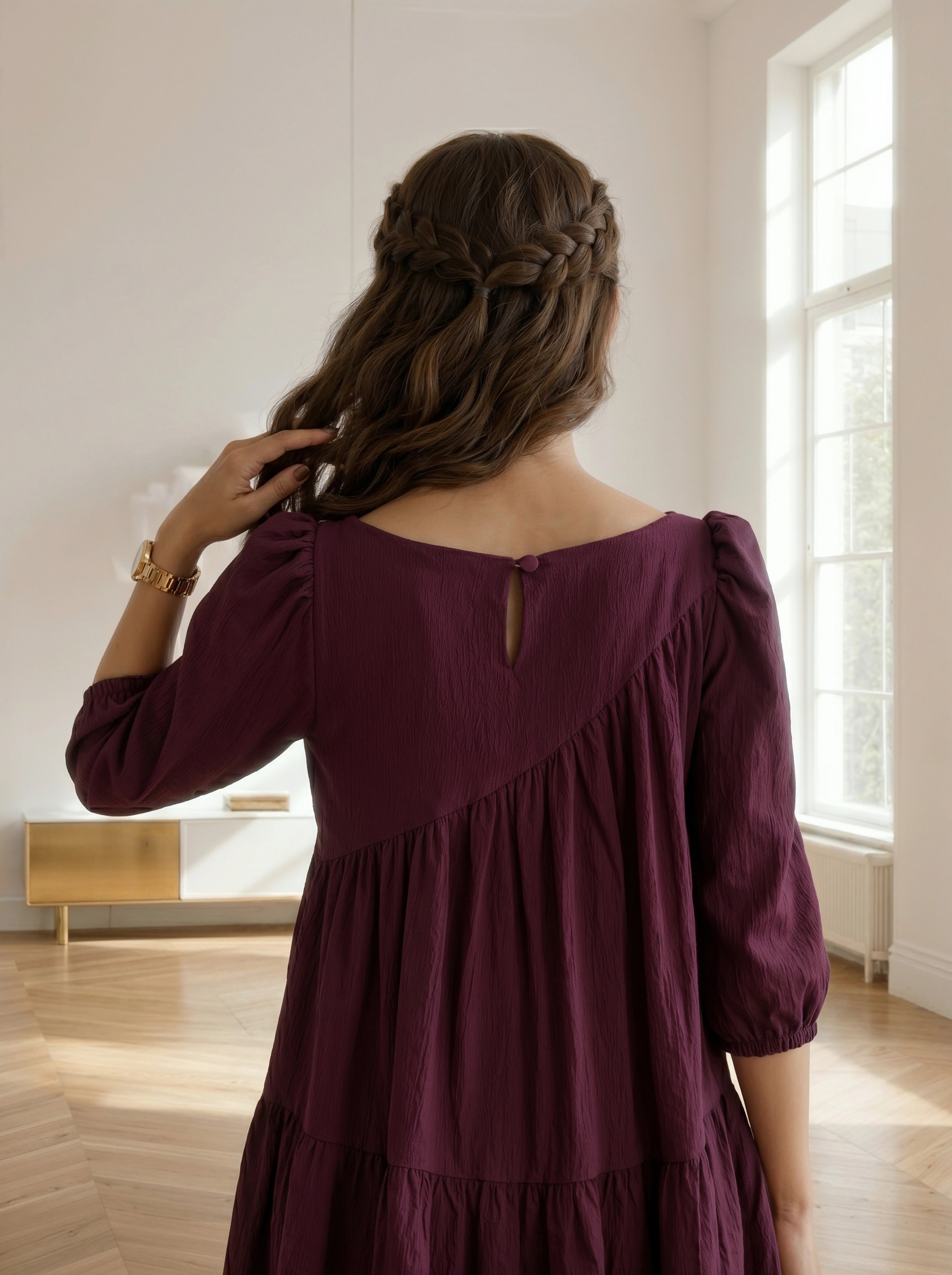 Woman in a burgundy dress standing in a room with a window in the background