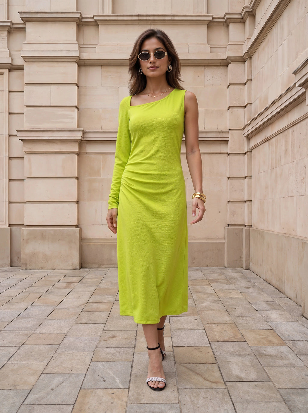 A woman wearing a bright lime green long-sleeve midi dress with a draped, ruched bodice, standing in front of a beige stone building.