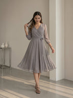 Woman wearing a gray patterned dress in a minimalistic room.
