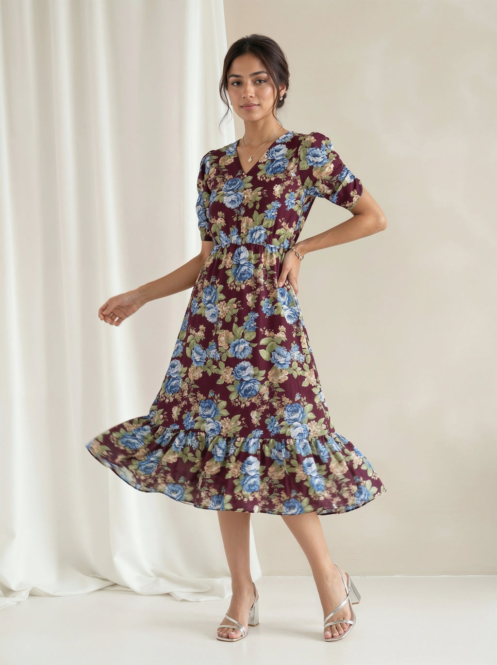 A woman modeling a blue tiered midi dress with a textured chevron pattern, standing in a bright, sunlit white room with large windows.