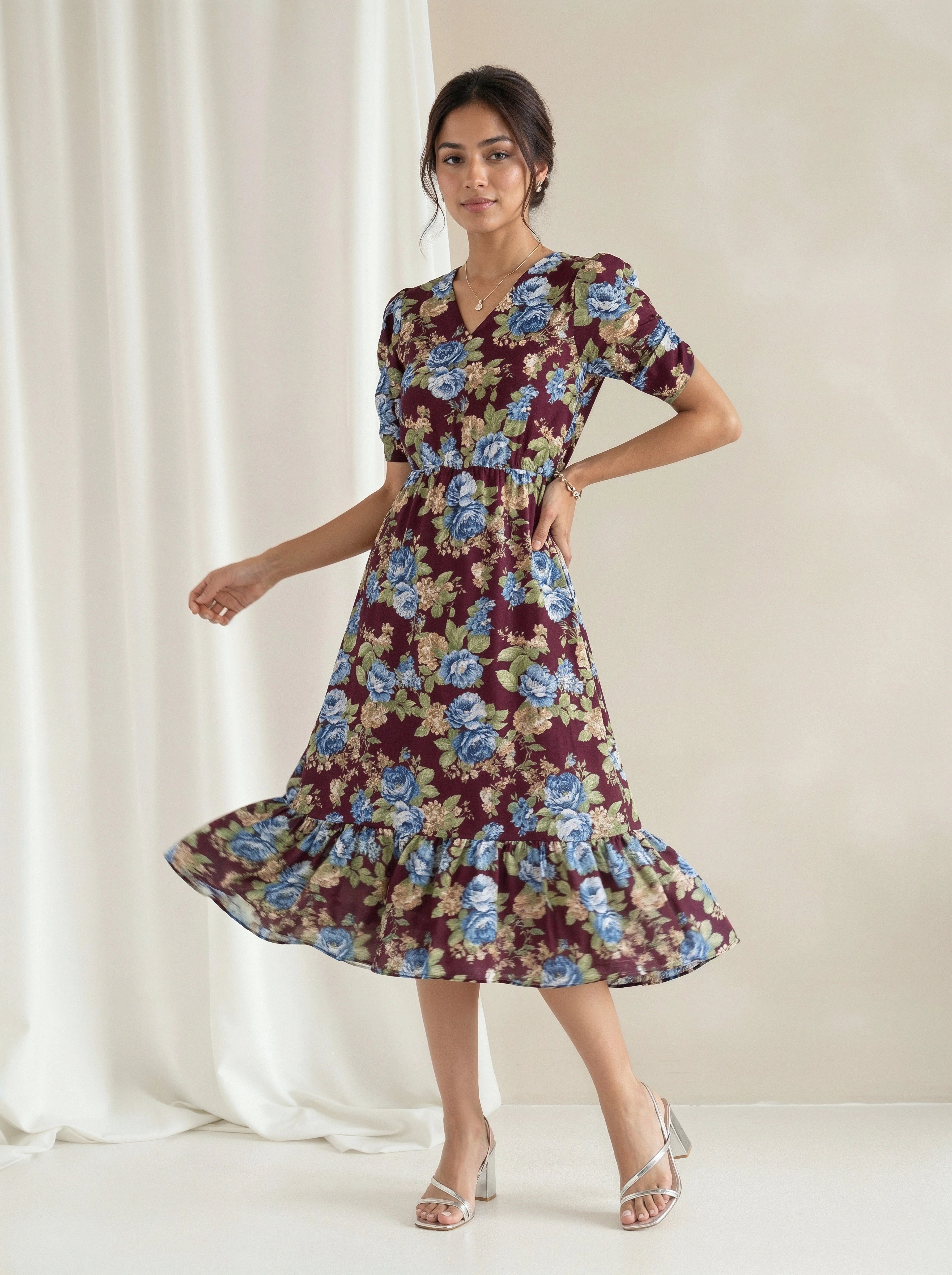 A woman modeling a blue tiered midi dress with a textured chevron pattern, standing in a bright, sunlit white room with large windows.