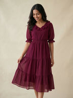 Woman wearing a burgundy dress with ruffled sleeves and layered skirt on a beige background
