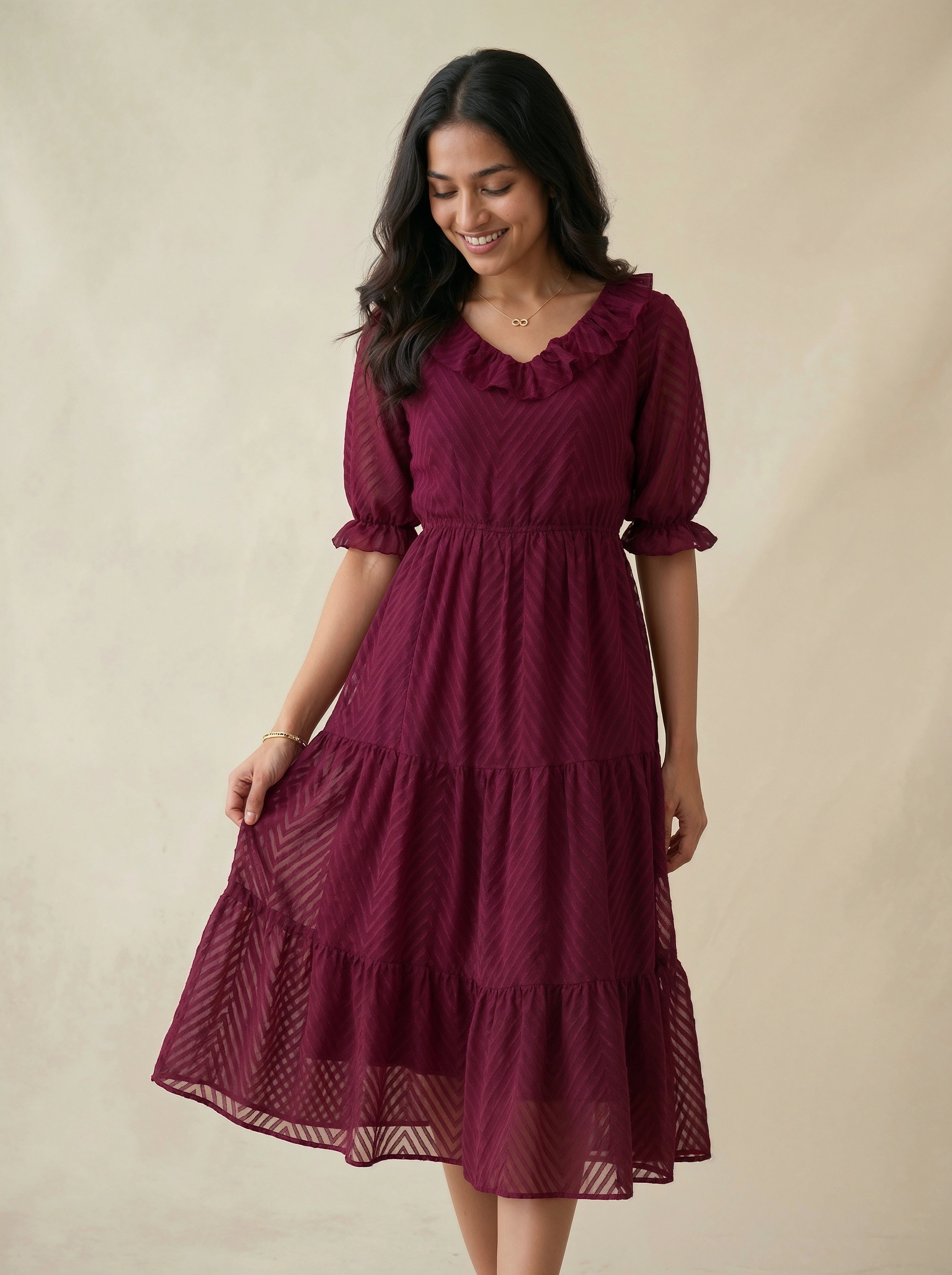 Woman wearing a burgundy dress with ruffled sleeves and layered skirt on a beige background