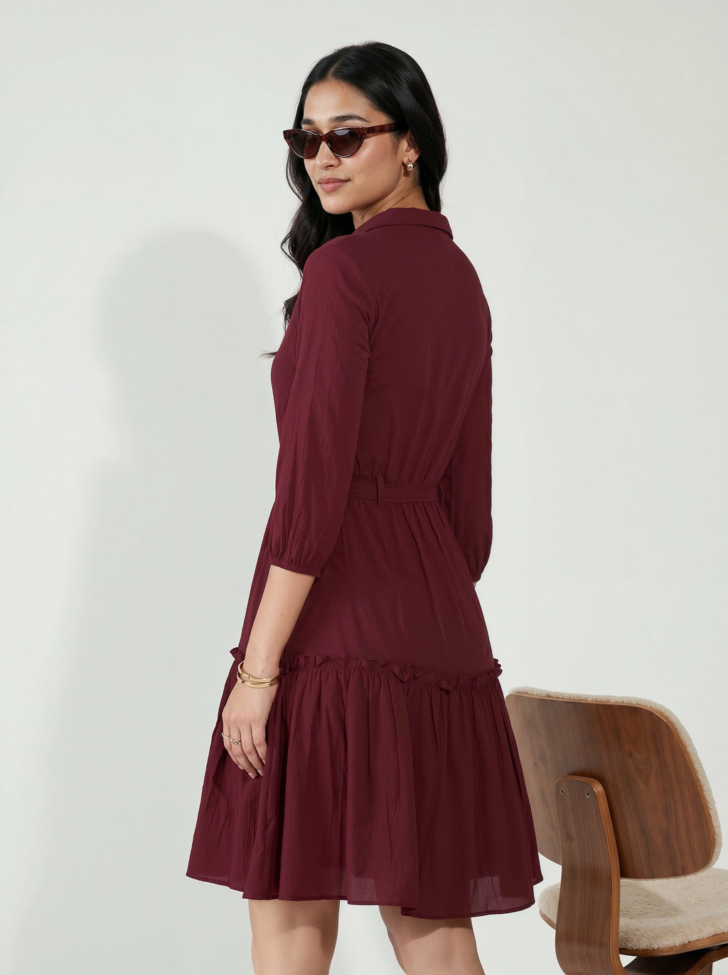 Woman wearing a burgundy dress with a wooden chair in the background