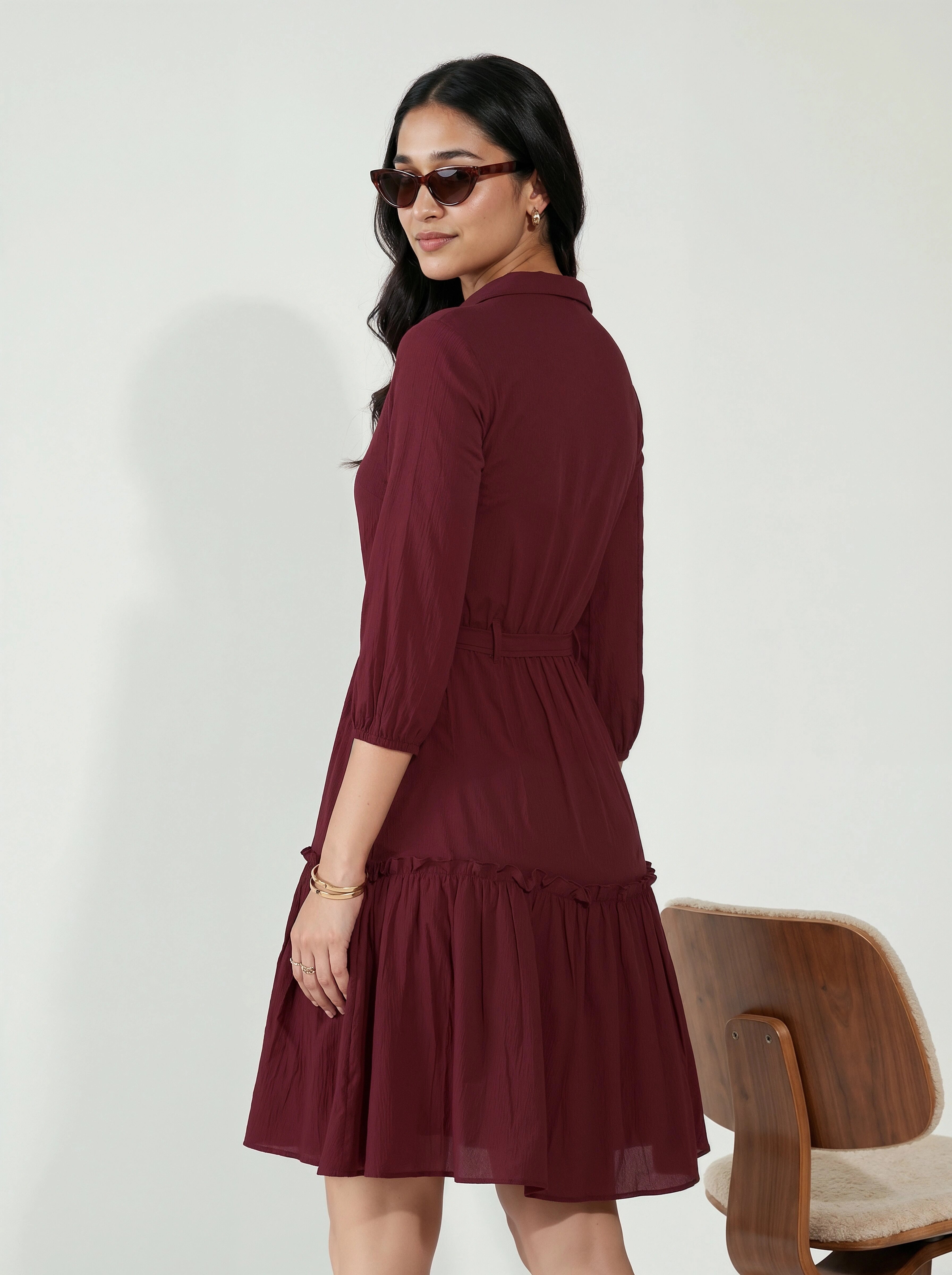 Woman wearing a burgundy dress with a wooden chair in the background