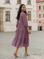 Woman in a purple dress standing on a cobblestone street with buildings in the background