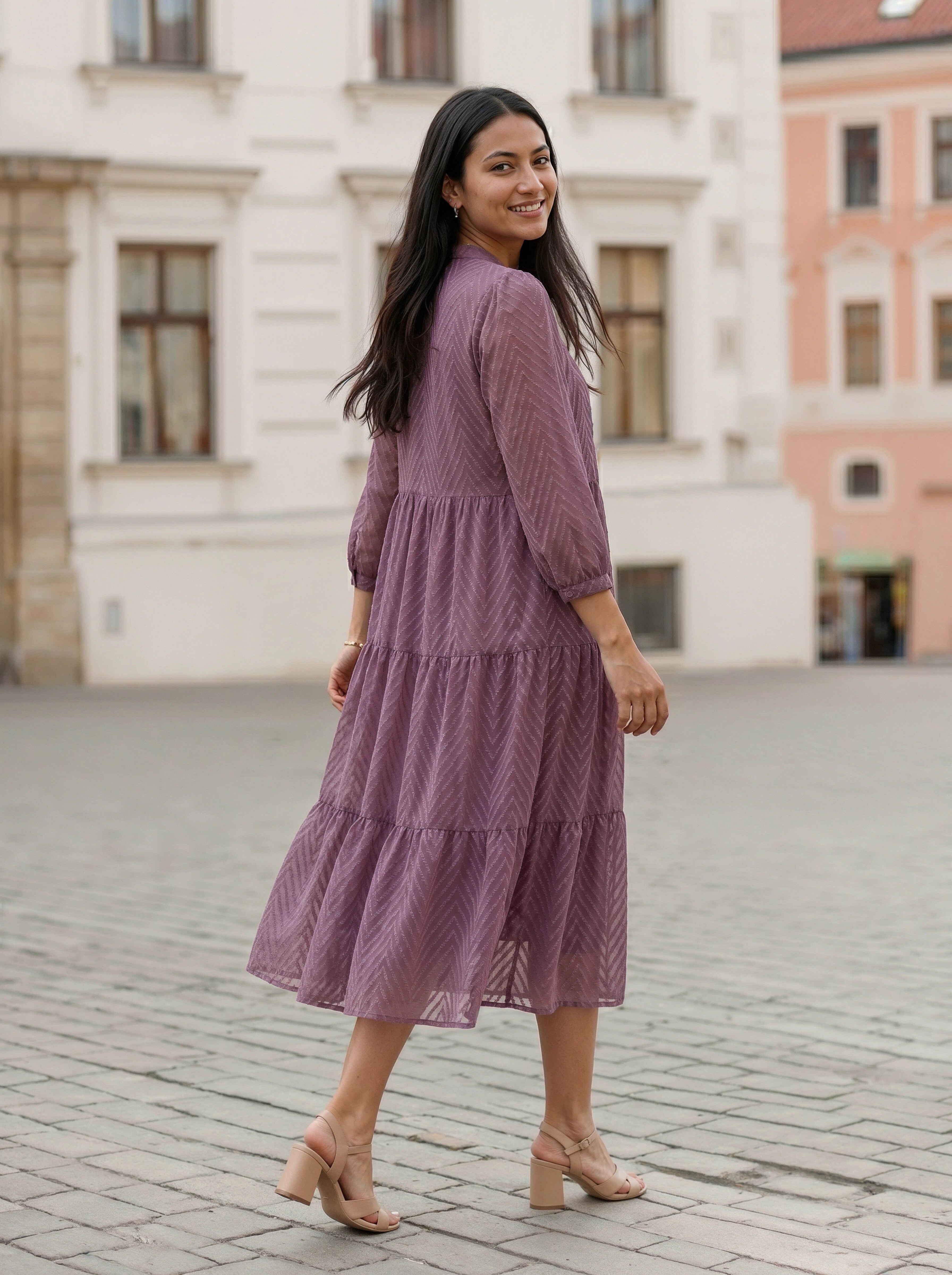 Woman in a purple dress standing on a cobblestone street with buildings in the background