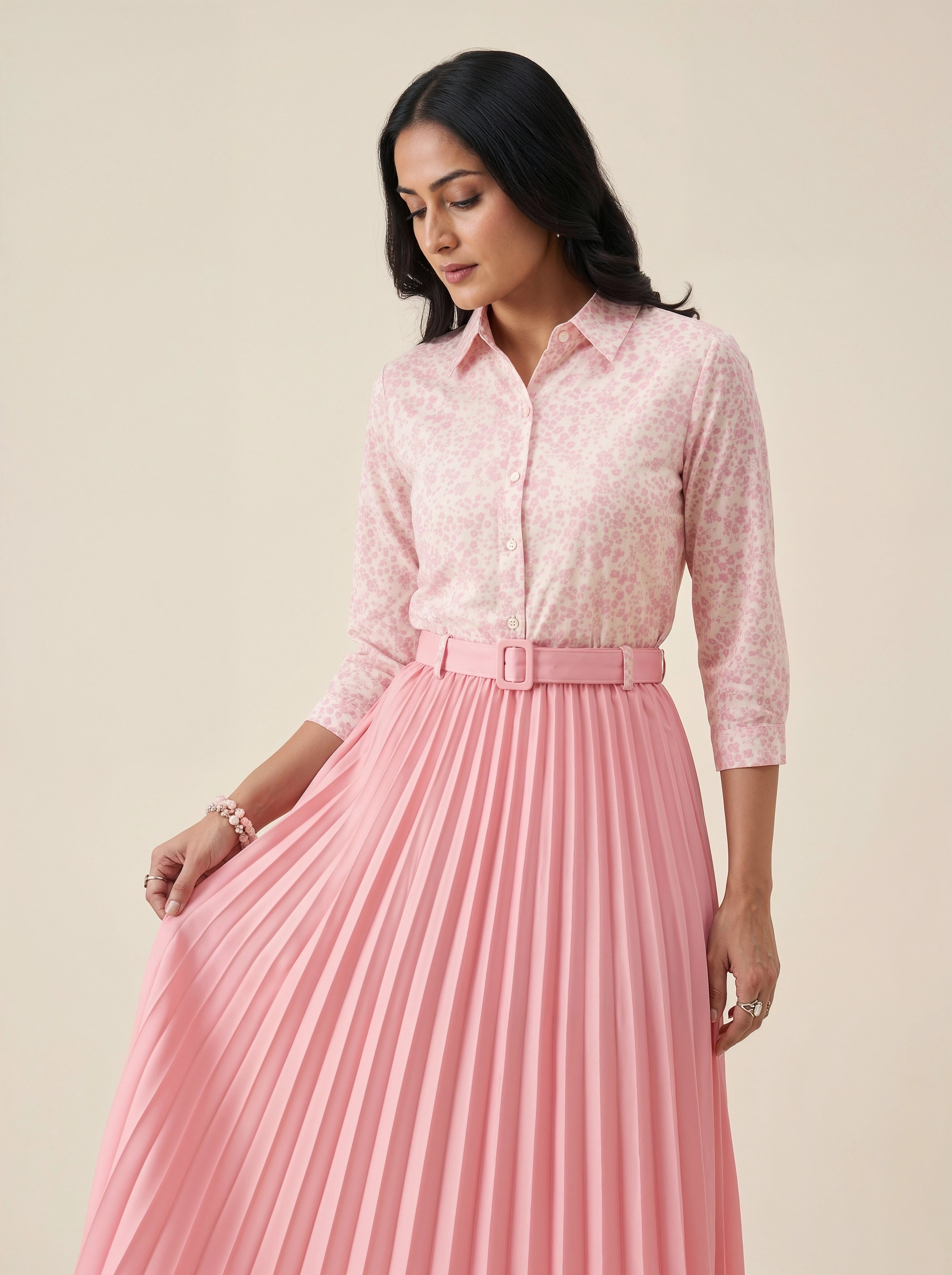Woman wearing a pink floral blouse and pleated pink skirt on a beige background